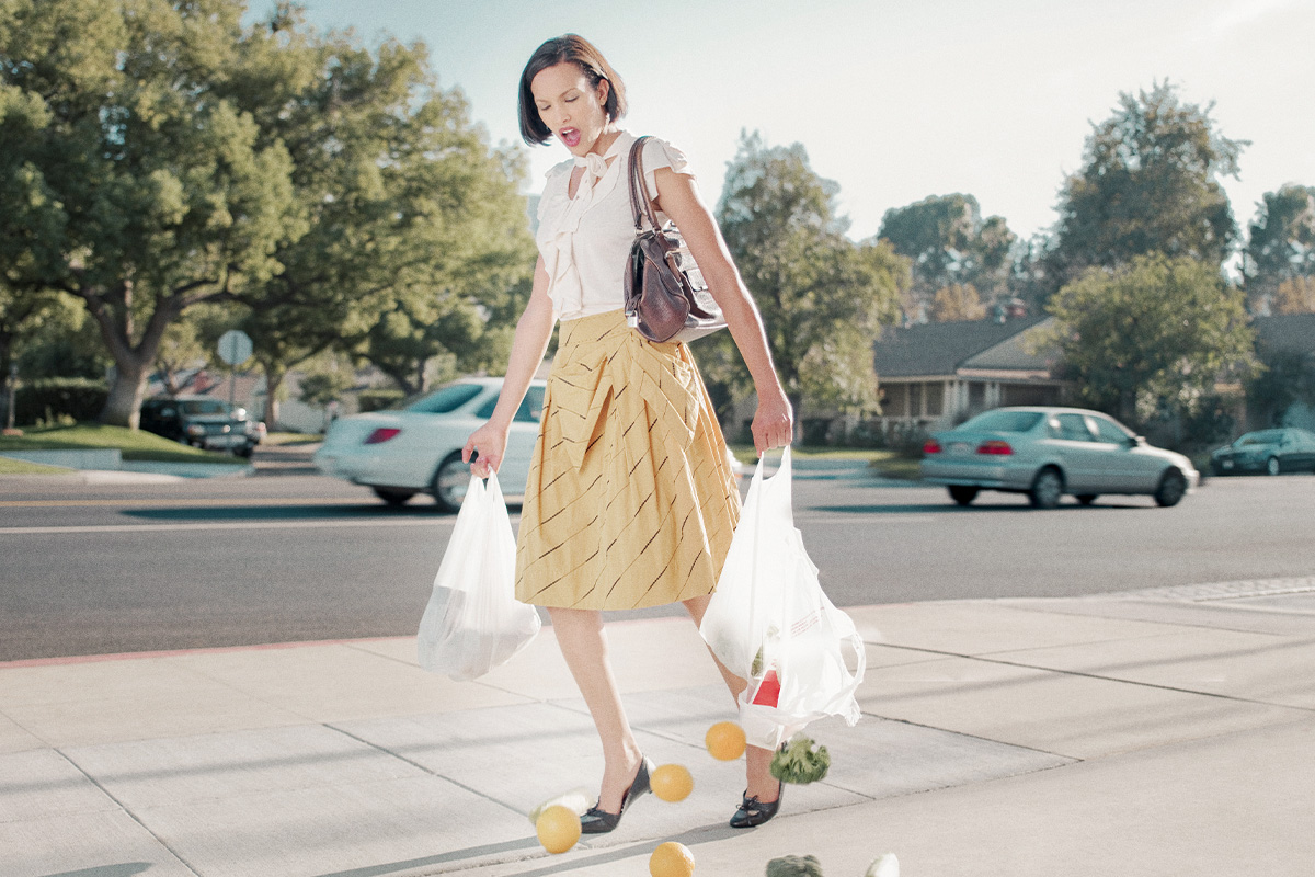 Woman holding ripped grocery bags with fruit falling out of them